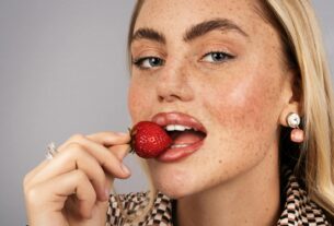 Close-up portrait of a blonde woman holding a strawberry near her lips.