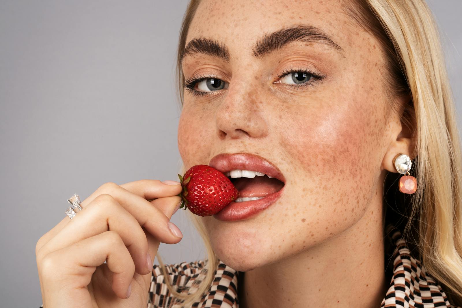 Close-up portrait of a blonde woman holding a strawberry near her lips.