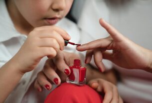 A close-up of a child painting their mother's fingernails red, showcasing a bonding moment.