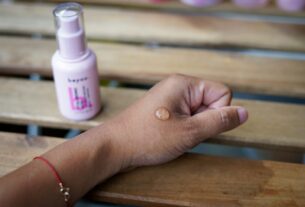 a woman's hand holding a bottle of sunscreen on a wooden bench